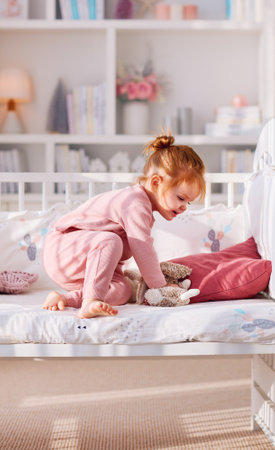 cute toddler baby girl having fun playing stuffed toys on the bed in nursery roomの写真素材