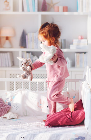 cute toddler baby girl having fun playing stuffed toys on the bed in nursery roomの写真素材
