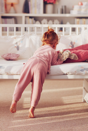 rear view of toddler baby girl playing toy on the bed in nursery room at homeの写真素材