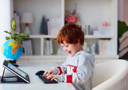 happy redhead kid typing on keyboard, studying on laptop at home