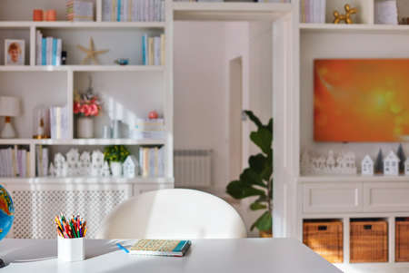 sunlit cozy home office interior with wooden furniture, white desk with coloured pencilsの写真素材