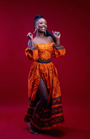 beautiful happy african woman in traditional dress dancing on red background, studio shot