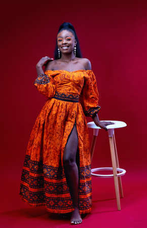 beautiful happy african woman in traditional dress posing on red background, studio shotの写真素材