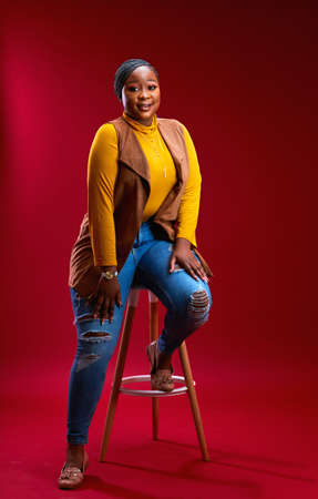 confident plus size african woman posing on chair in studioの写真素材