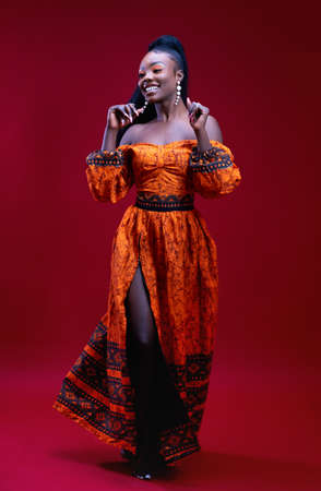beautiful happy african woman in traditional dress dancing on red background, studio shotの写真素材