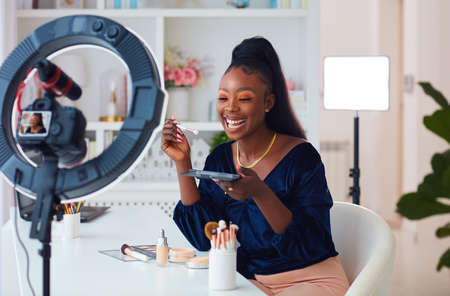 happy young african american woman streaming a beauty vlog from home, online content creator applying a makeup onの写真素材