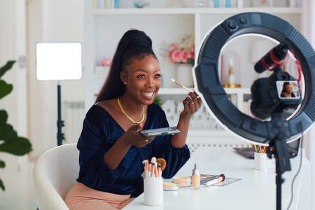 happy young african american woman streaming a beauty vlog from home, online content creator applying a makeup onの写真素材