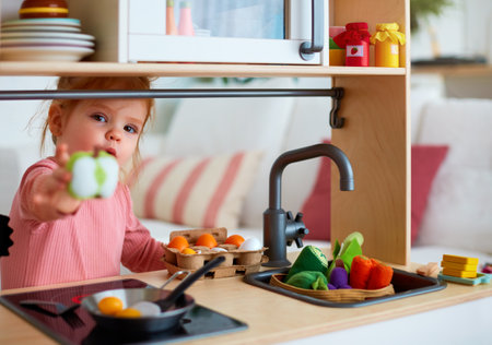 cute toddler baby girl playing on toy kitchen at home, roasting eggs and treat you with apple slice, let's shareの写真素材