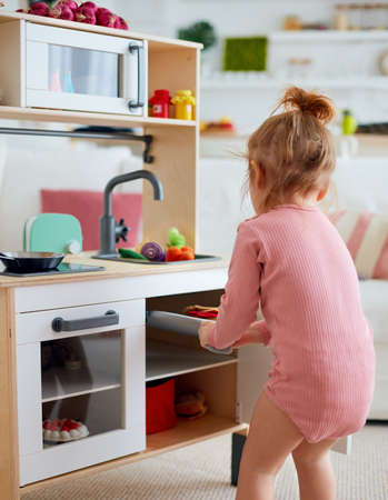 toddler baby girl playing on toy kitchen at homeの写真素材