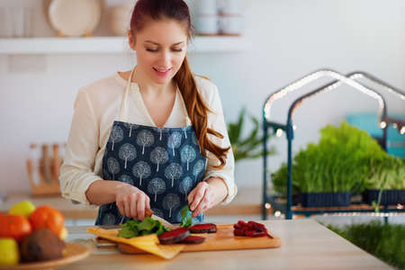 woman cutting beetroot and spinach leaves for organic raw salad at the kitchen with micro green cultivation on background, healthy vegan nutritionの写真素材