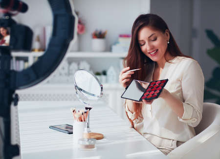beautiful young woman streaming a beauty vlog from home, online content creator applying a makeup onの写真素材