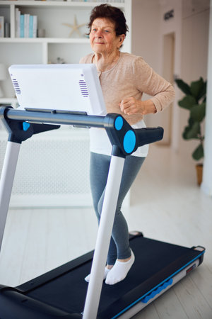 active mature woman running on treadmill at home, sporty lifestyle, 84 years old lady