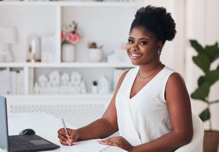 cheerful young woman sitting at the desk, writing and studying at homeの写真素材