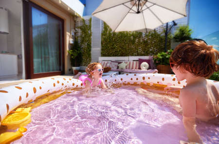 excited kids having fun in inflatable swimming pool at home patio at sunny summer dayの写真素材
