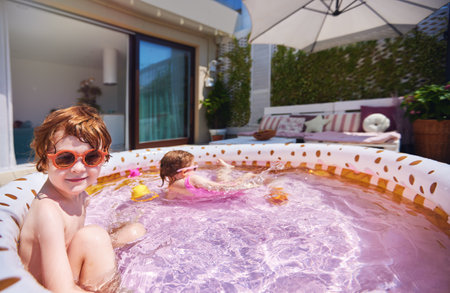 cute kids having fun in inflatable swimming pool at home patio at sunny summer dayの写真素材