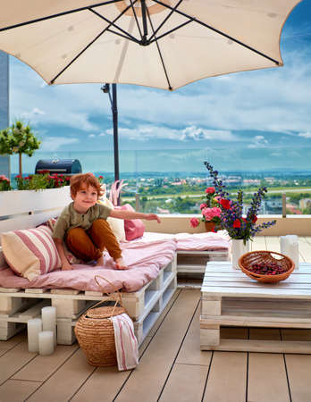 smiling kid relaxing on lounge area made of wooden pallets, summer outdoor patioの写真素材