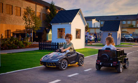 happy kids are driving the electric toy cars, moving around the toy city at the playgroundの写真素材