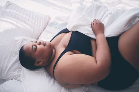 young, plus size woman sleeping peacefully in bed in the morningの写真素材