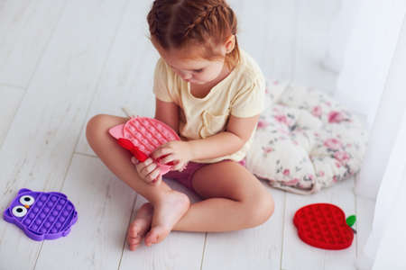 toddler baby girl playing with colorful sensory toys. pushing the bubles on pop it fidget toyの写真素材