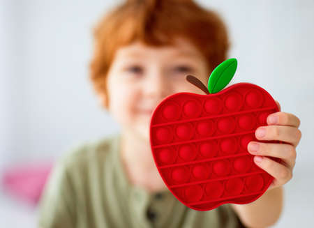 excited happy kid holding a vibrant sensory toy, pop it fidget toy in apple shapeの写真素材