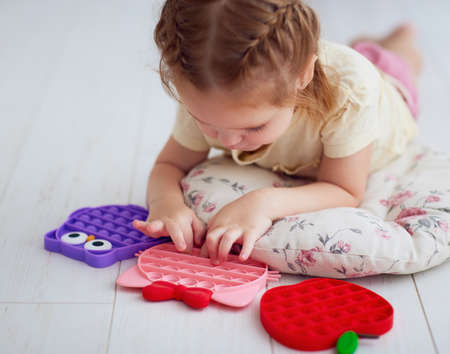 happy baby girl playing with colorful sensory toys. pushing the bubles on pop it fidget toyの写真素材