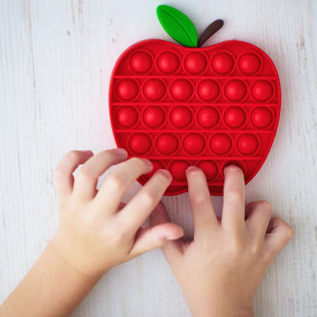 figers of toddler kid are pushing the bubbles on sensory toy, trendy pop it fidget toy in apple shapeの写真素材