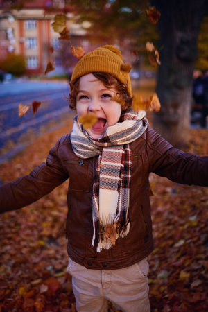 delighted young boy having fun on a walk in autumn city, throwing and catching fallen leavesの写真素材
