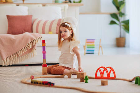 cute redhead baby girl playing on the carpet at home, stacking colorful wooden blocks, building a towerの写真素材