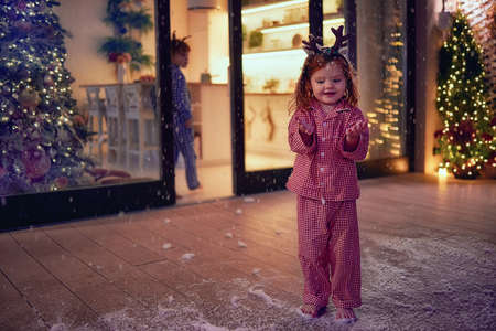happy toddler baby girl catching snowflakes at the patio on Christmas night. kids having fun at home during winter holidaysの写真素材