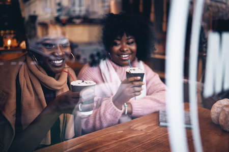 Happy Friends, Laughing African American Women Sitting in Cozy Cafe on Winter Holidaysの写真素材