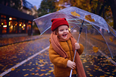 happy baby girl with umbrella on the walk in the autumn city, cozy warm clothingの写真素材