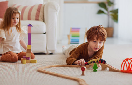 cute redhead kids, siblings having fun, playing with wooden toys on the carpet at homeの写真素材