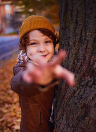 delighted redhead young boy having fun on a walk in autumn city, trying to reach youの写真素材