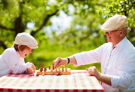 happy grandpa and grandson playing chess in spring gardenの写真素材
