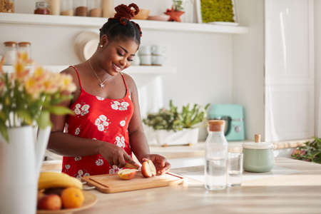 happy young woman cooking on the kitchen at home in sunny roomの写真素材