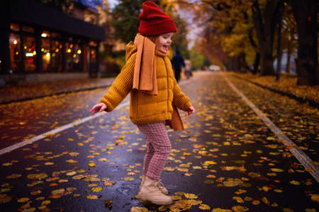 happy redhead baby girl having fun on the walk in the autumn city, cozy warm clothingの写真素材
