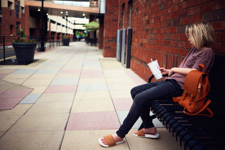 teenage boy with a soft drink sitting on a bench outsideの写真素材
