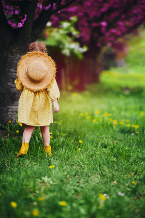 cute baby girl is having fun, walking on blooming meadow in spring gardenの写真素材