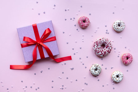 Pink gift box with red ribbon bow. Holiday present. Pink background with donuts.の写真素材
