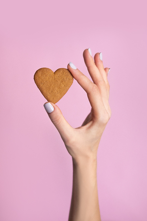Young woman hand holding biscuit isolated on pink background.の写真素材