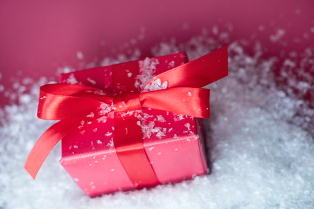 Small gift with red bow in snow on red background. Free space for your text.の写真素材