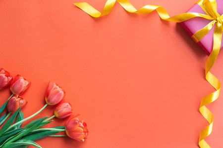 Holidays concept. Beautiful tulips and gift box on orange background. Copy spaceの写真素材