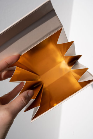 Hand holding an open accordion-folded gold paper box