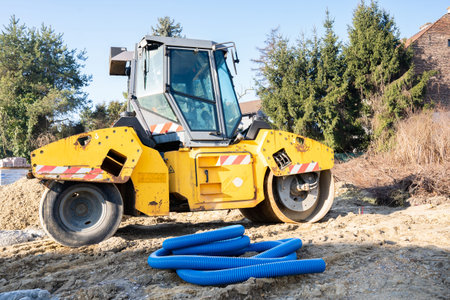 A yellow road roller at a construction site next to a blue corrugated pipe