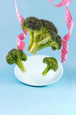 Flying foods, concept of lightness and healthy eating. Green juicy broccoli and a tape for measuring the waist on a blue background. Space for text, front view.の写真素材