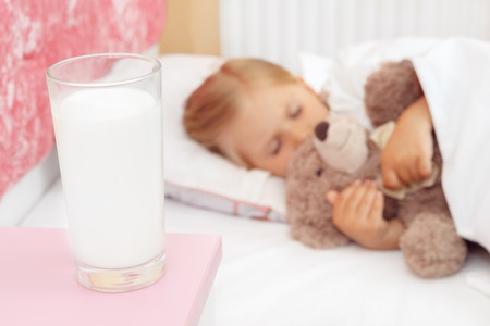 Adorable little girl sleeping in bed with her teddy bearの写真素材