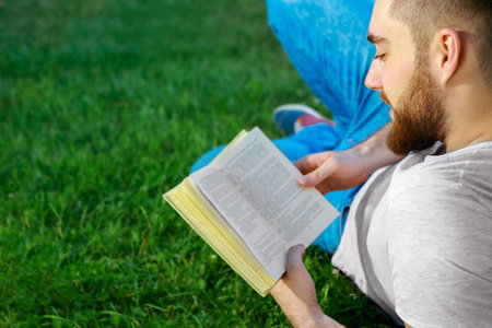 Young man reading a book in park. Lying on the grass.