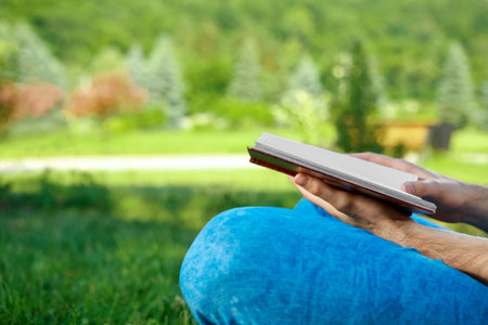 Young man reading a book in park. Lying on the grass.