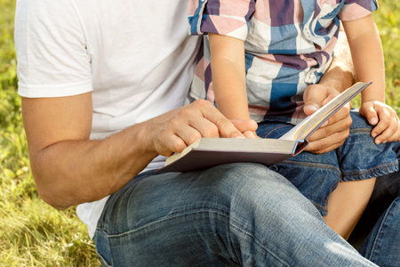 Father and son reading book in park