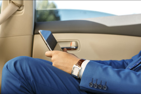 Young businessman sitting in the back-seat of a car, using his digital tablet